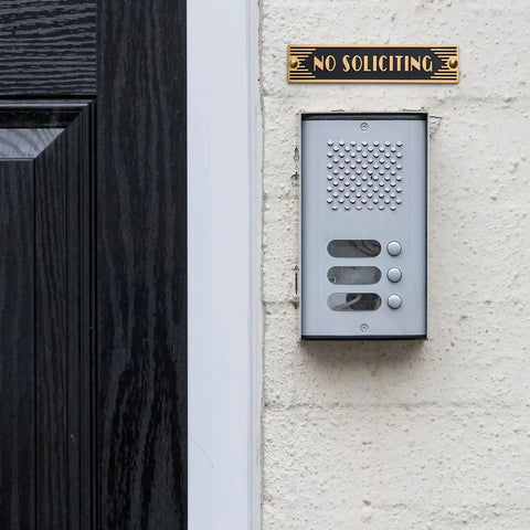 Brass No Soliciting Sign Six Point Five Inch Classic Art Deco Style With Brushed Matte Finish next to a doorbell on a wall.
