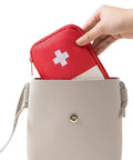 Hand placing a Must Have Emergency First Aid Bag Grab And Go Medical Kit into a beige handbag.
