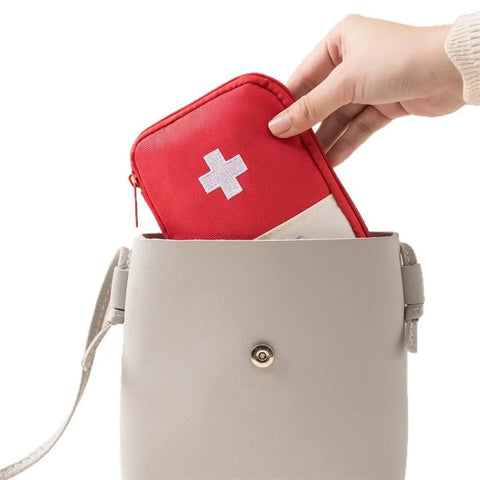 Hand placing a Must Have Emergency First Aid Bag Grab And Go Medical Kit into a beige handbag.