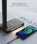 Close-up of LED desk lamp with wireless charger, USB port showing 5V-2.1A, and phone charging on pad.