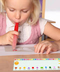Child using a blow pen at a desk with alphabet and shape chart, focused on creating art. 36 Pack Transparent Self-Adhesive Nameplate Pockets For Desks, 18.9 X 4.7 Inches, 7 Mil Thick, Sticky Name Tag Pockets - Durable, Easy Peel, Ideal For Office Signage, Events, And Organization.