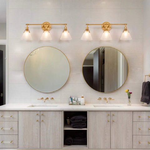 Three Light Gold Vanity Light Fixtures With White Frosted Glass Shades Over Mirror In Brushed Antique Gold Finish above bathroom sinks