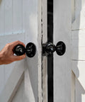 Hand using Built Tough Heavy Duty Matte Black Barn Door Pull Handle Solid Zinc Alloy Ring Knob on white double doors.