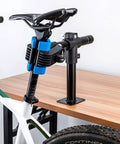 Heavy Duty Bike Repair Stand With Bench Mount attached to wooden workbench, clamping a bike seat post.