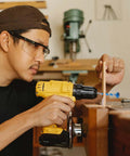 Cordless yellow drill with blue hole-opening bit drilling wood (side view)