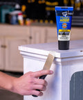 Person applying DIY Friendly All Purpose Latex Wood Filler White 6 Oz For Cracks Holes And Gouges to a wooden corner