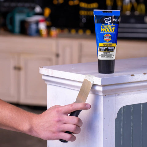 Person applying DIY Friendly All Purpose Latex Wood Filler White 6 Oz For Cracks Holes And Gouges to a wooden corner