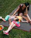 Family relaxing outdoors on Waterproof Camping Tarp Groundsheet Footprint 51.2 X 83 Inches with fruit nearby on grass.