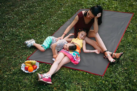 Family relaxing outdoors on Waterproof Camping Tarp Groundsheet Footprint 51.2 X 83 Inches with fruit nearby on grass.