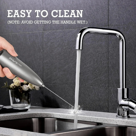 Handheld Milk Frother With Stand, Electric Foam Maker With Stainless Steel Whisk being rinsed under a faucet, gray finish, easy clean