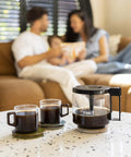 1.25L Glass Carafe for KBG Brewers, Clear Black Version, on table with cups in modern living room setting.