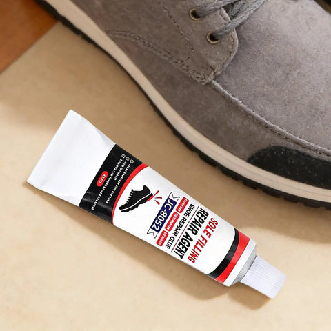 Tube of All Purpose Quick Dry Shoe Glue For Sneakers Boots And Sandals, shown next to a gray sneaker, on a beige surface.
