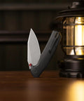 Folding Pocket Knife With A 3.34 Inch Blade And Button Liner Lock, open beside a lantern, showing PVD coated steel blade.