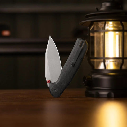 Folding Pocket Knife With A 3.34 Inch Blade And Button Liner Lock, open beside a lantern, showing PVD coated steel blade.