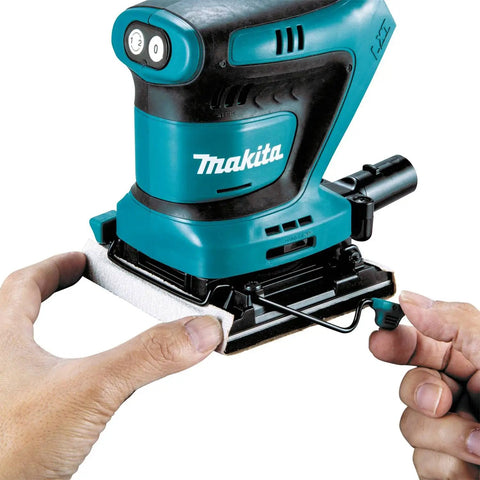 Hands attaching paper to 18V Cordless 1/4 Sheet Finishing Sander With Two Speed Control 11K And 14K OPM Uses Four And A Half Inch By Four Inch Abrasive Paper Large Clamping Lever Tool Only