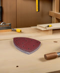 Merryhappy 60pcs Triangle Mouse Detail Sander Sandpaper Sheets with 11-Hole Hook and Loop Backing on a woodworking bench.