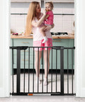 Extra Wide Walk Through Pet Gate With Auto Close Durable Metal Baby And Pet Gate For Stairs And Doorways Forty Point Five Inches Full Width Includes 2 Extension Kits Black installed in doorway with mother holding child in kitchen