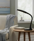 Natural Daylight Desk Lamp With Adjustable Gooseneck For Reading Working Crafting Sewing Or Homework Eye Strain Relief 6400K 27W Light For Dorm And Office Black next to a chair in a cozy room setting.