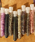 Ten clear plastic test tubes filled with various colored beads, with caps in a straight line on a textured surface.
