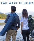 Rear view of two people carrying Oversized Folding High Back Lawn Chair for Adults With Cup Holder and Carrying Strap by a lake.