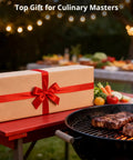 Gift-wrapped box on table beside charcoal grill with steaks in a garden setting, labeled as top gift for culinary masters.