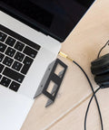 Heavy Duty Laptop Stand And Tablet Mount Under Desk Organizer Rack Black next to a laptop and headphones on a wooden desk.