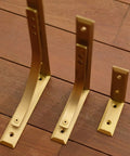 Heavy Duty Shelf Brackets Wall Mount Kickass Brass Metal Supports showing three sizes on wooden surface, ideal for strong floating shelves.