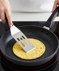 Small stainless steel slotted spatula flipping pancake in nonstick frying pan