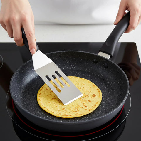 Small stainless steel slotted spatula flipping pancake in nonstick frying pan