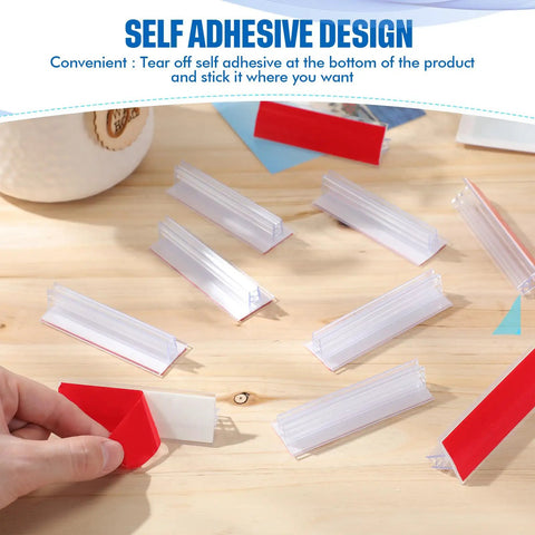 30 Pack 3x1 Inch Sneeze Guard Gripper Sign Holders With Adhesive For Desks, Shop Floor Displays, Wall Mounts, Store Vendor Events, Warehouse, Clear Great For Counters, Displays And Shelves On The Shop Floor. Self-adhesive clear plastic sign holders on a wooden counter