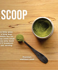 Top view of matcha powder in a tin with a premium stainless steel scoop on a wooden surface