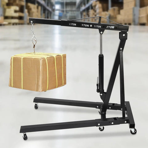 Built Tough Two Ton Hydraulic Engine Hoist With Folding Cherry Picker Design And Integrated Stands To Roll Right Through Your Garage While Lifting Motors With Six Iron Caster Wheels Guaranteed To Get The Job Done lifting a cardboard box in a warehouse setting.