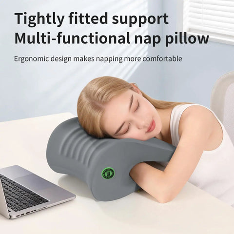 Woman resting on ergonomic gray nap pillow by desk, providing neck and head support.