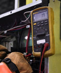 Technician with gloves using multimeter at job site for safety compliance