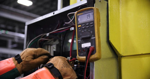Technician with gloves using multimeter at job site for safety compliance