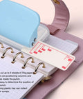 3 Hole Paper Punch Handheld, 5 Sheets Capacity, Metal Body With Slipproof Grip And Plastic Cover in use on B5 paper