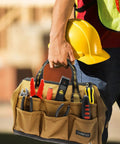 Construction worker holding Wide Mouth 14 Inch Tool Bag Gear Bag For Plumbers Electricians And DIY Handymen With Heavy Duty 900D Polyester Build Also Great For Daily Office Use Travel Camping And Fishing Tan, filled with tools, wearing safety gear.