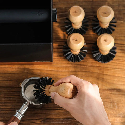 Hands using 58mm Portafilter Cleaning Brush For Espresso Machines Pro Barista Tool With Arc Bristle Design on portafilter basket.