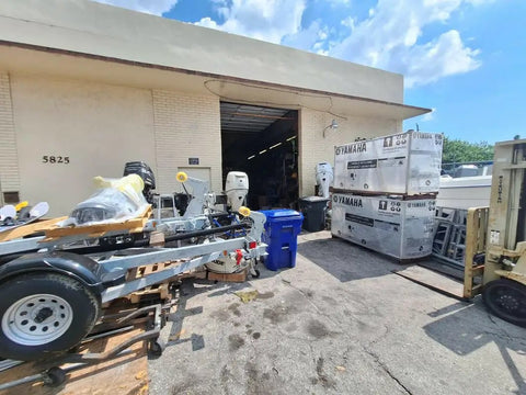 Outdoor warehouse scene with various equipment, including palletized motors and metal frames, under a clear sky; no specific product visible.