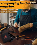 Man working with leather tools, leather storage box in foreground, on workshop table with stitching punches and cutting knife.