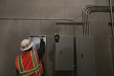 Boss Class 12V Max Three Plane Green Beam Laser Level in use on a construction site for precise alignment of electrical boxes.