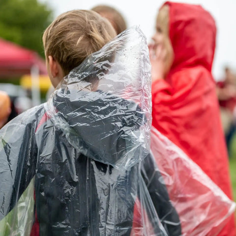 Kids wearing clear and red disposable ponchos with hoods for rainy days, perfect for school trips. Kids Rain Ponchos Pack Of 20