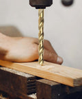 Close-up of a gold-colored cobalt twist drill bit in a drill chuck drilling into a wooden plank clamped in a vise