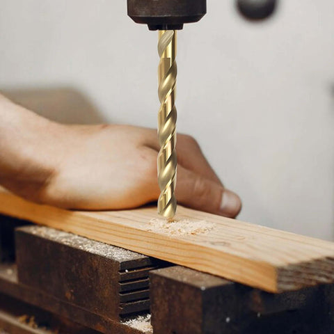 Close-up of a gold-colored cobalt twist drill bit in a drill chuck drilling into a wooden plank clamped in a vise