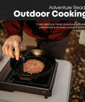 Person cooking meat on 10,000 BTU Dual Fuel Camp Stove For Butane And Propane Portable Outdoor Grill with cast iron pan