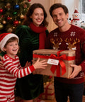 Family in festive attire holding a Christmas gift box with a red ribbon beside a decorated tree and snowman in the background.