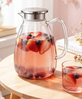 2.2L Glass Pitcher With Lid And Handle, Borosilicate Water Carafe, Stainless Steel Dual Filter Lid, Heat Resistant For Hot And Cold Bevs Like Iced Tea, Coffee, Juice, And Cold Brew filled with fruit-infused water.