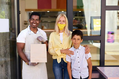Smiling man holding a Bulk 500 Pack Heavy Duty Kraft Paper Bags 10x13 Inches With Handles, standing with woman and child.