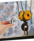 Heavy-duty cast-iron V-groove wheel held in hand; yellow double-pulley hoist assembly visible in background.