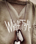 Person wearing a ball chain with dog tags, with "WHASETRAP" printed on the shirt.